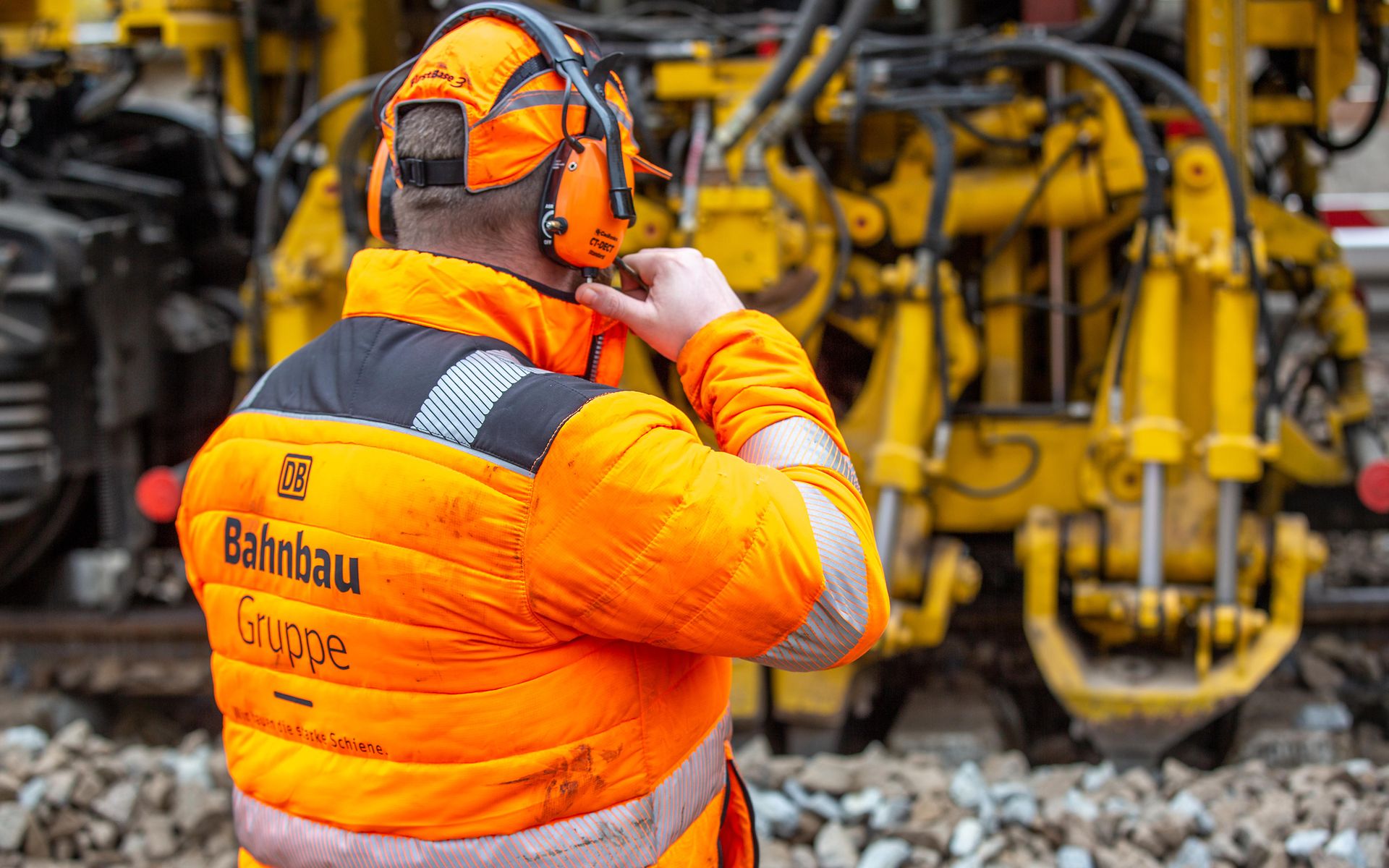 Man in orangefarbener Schutzausrüstung mit Blick auf eine gelbe Maschine