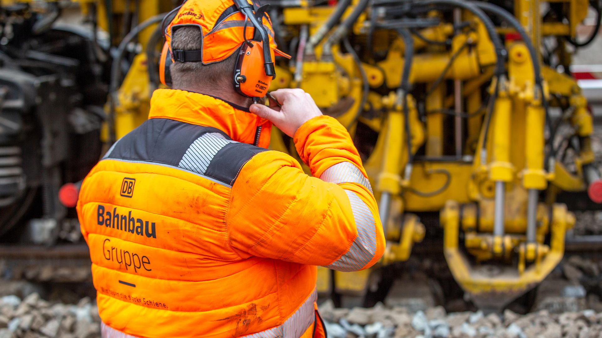 Man in orangefarbener Schutzausrüstung mit Blick auf eine gelbe Maschine