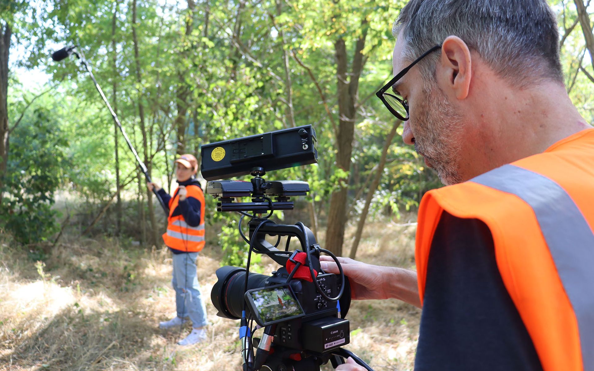 Zwei Mitarbeiter nehmen mit Kamera und Mikrofon einen Film in grüner Umgebung auf