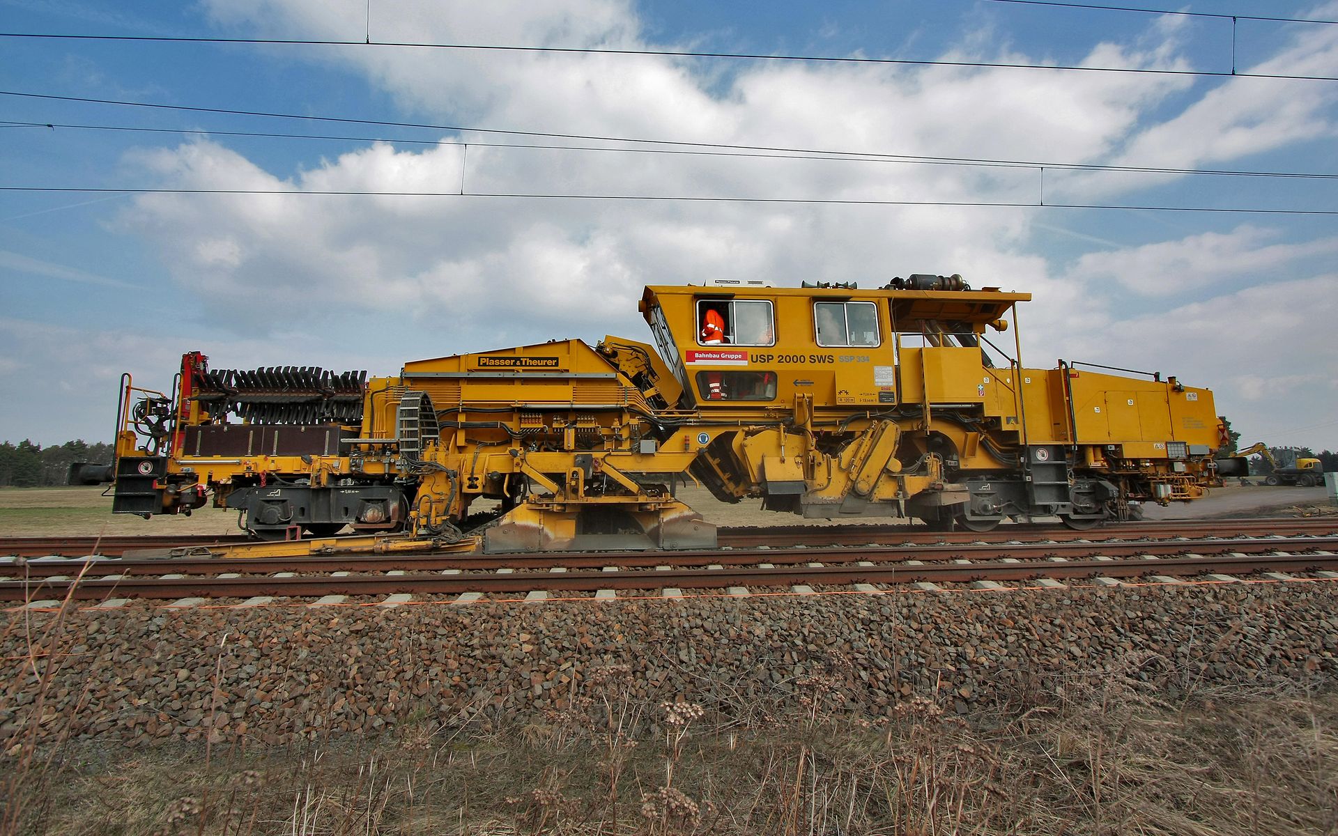 Universalschotterplaniermaschine auf einem Gleis bei leicht bewölktem Himmel