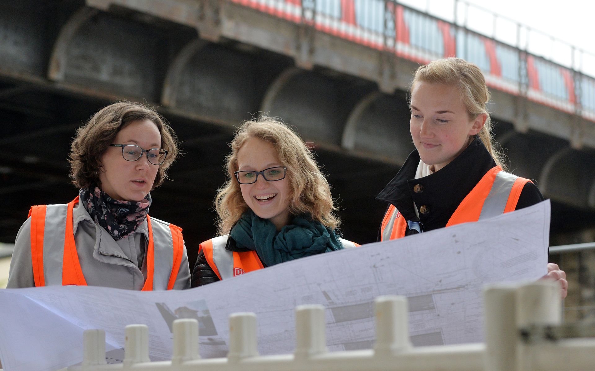 Drei Personen sehen auf großen Bauplan