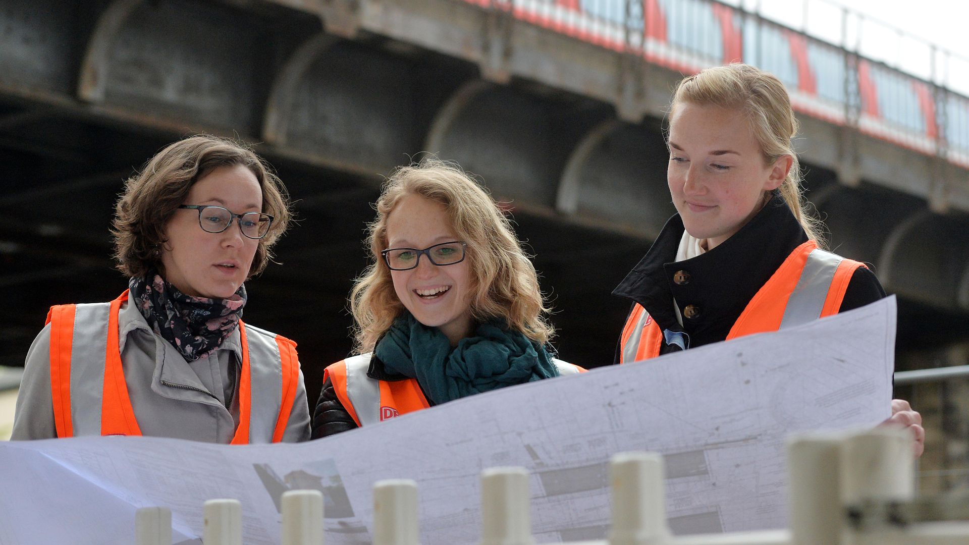Drei Personen sehen auf großen Bauplan