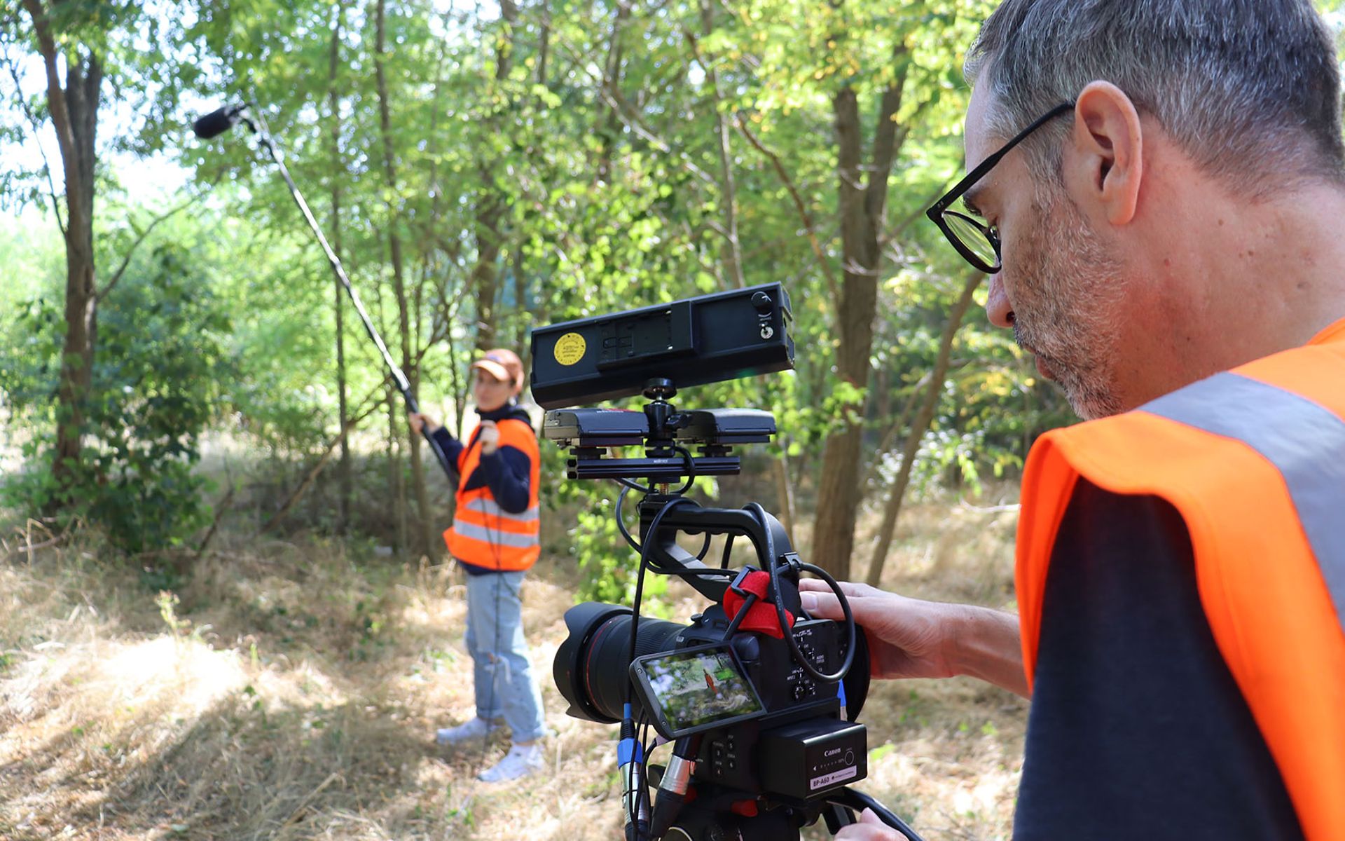 Zwei Mitarbeiter nehmen mit Kamera und Mikrofon einen Film in grüner Umgebung auf