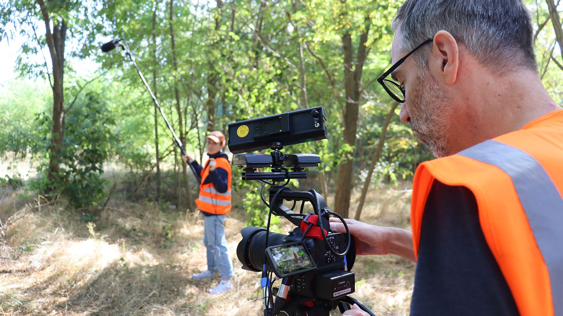 Zwei Mitarbeiter nehmen mit Kamera und Mikrofon einen Film in grüner Umgebung auf
