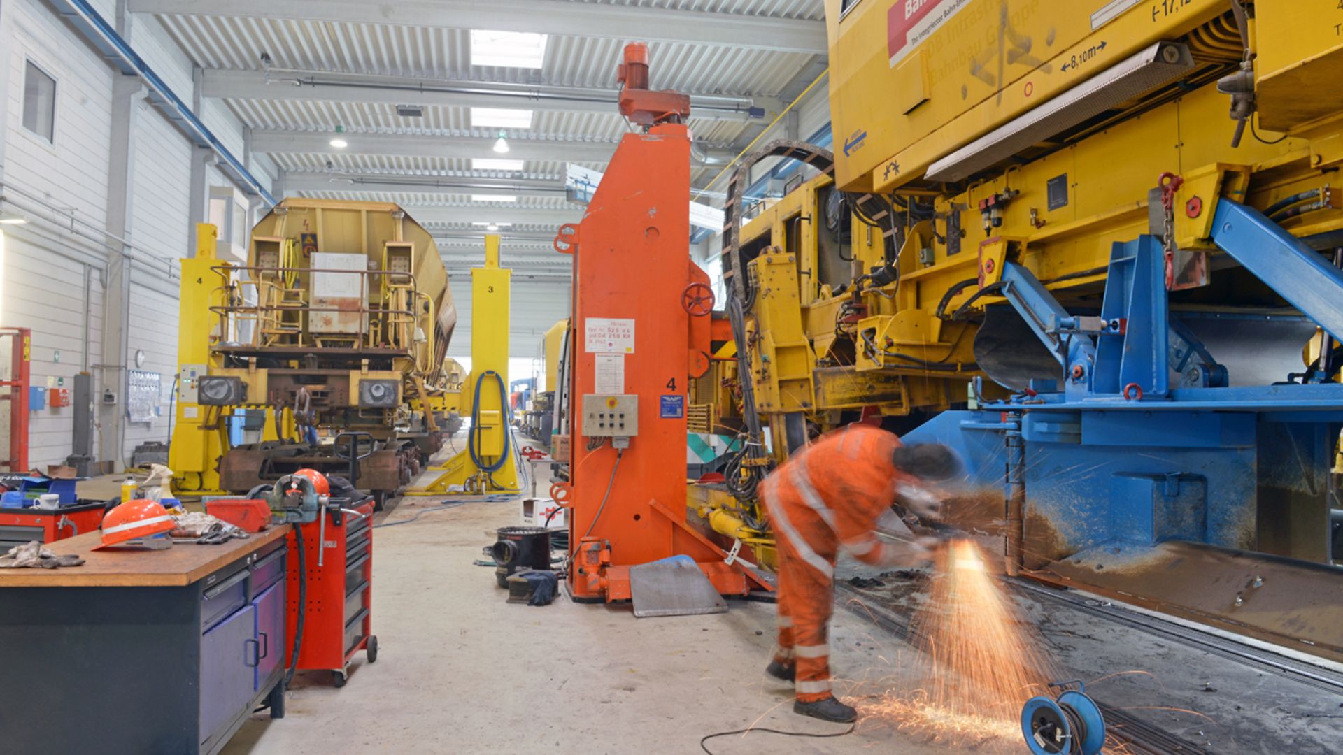 Mitarbeiter schweißt an einem gelben Bauwerkzeug in einer Werkstatt