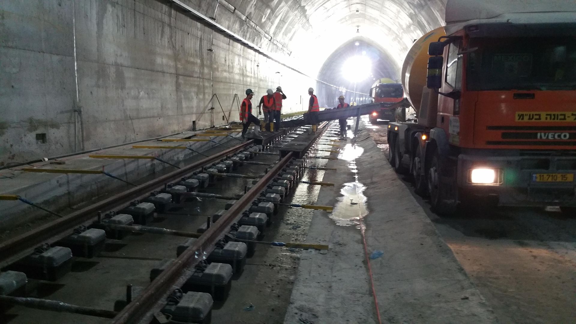 Mitarbeiter sind im Tunnel und verlegen eine Fahrbahn. Daneben sind zwei gelbe Betonmischfahrzeuge.