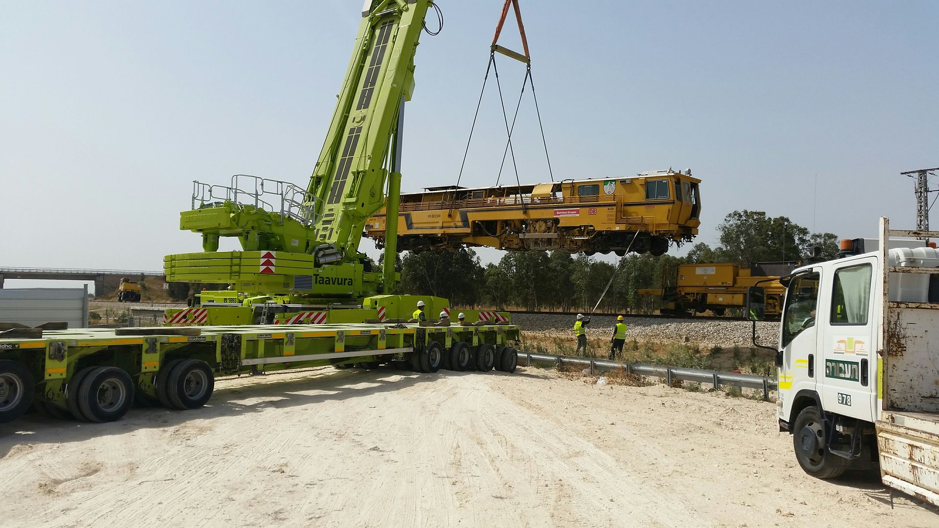 grüner Kran setzt gelbe Baumaschine auf Gleis