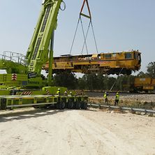 grüner Kran setzt gelbe Baumaschine auf Gleis