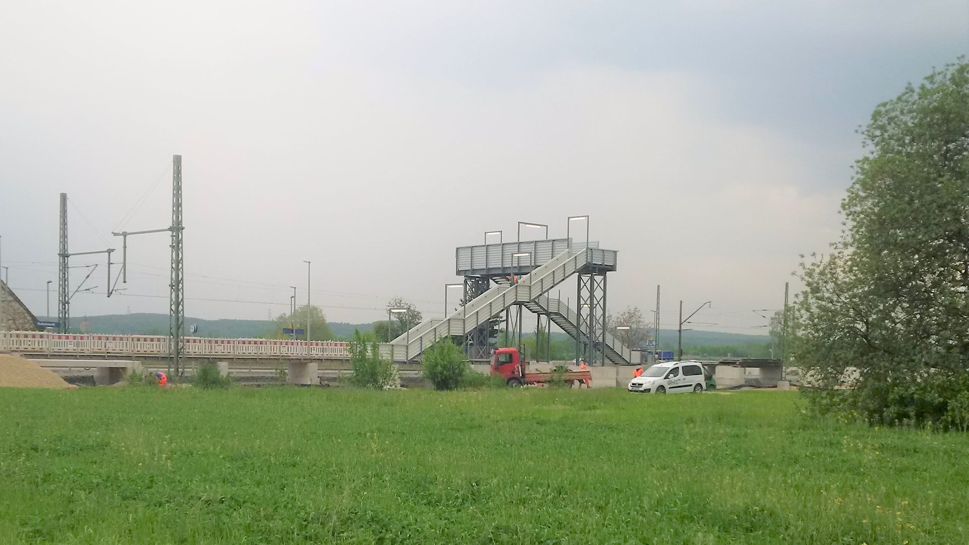 Grüne Wiese mit Fußgängerbehelfsbrücke im Hintergrund