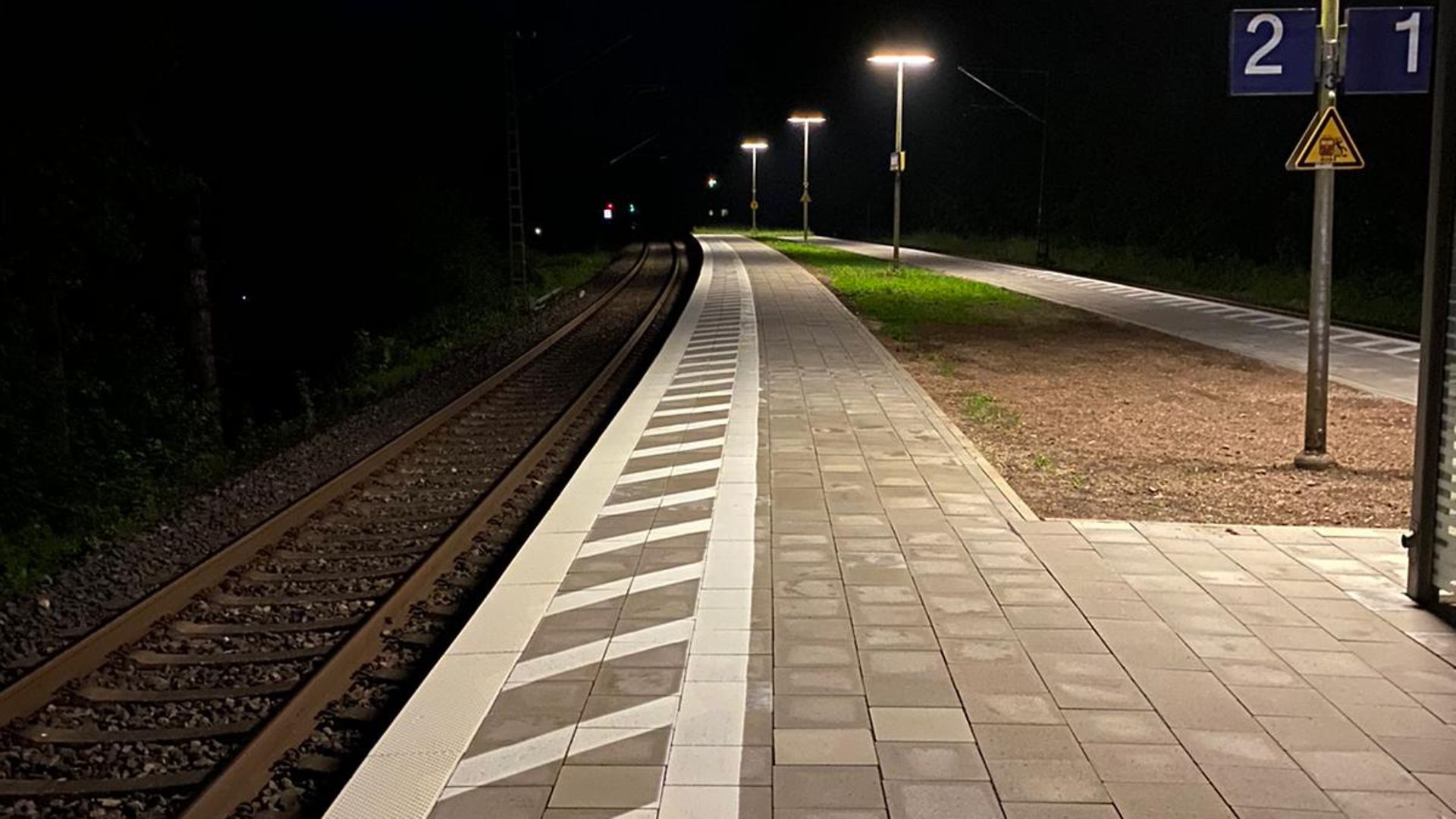Mittelbahnsteig mit drei Lampen und Blick auf Schiene bei Nacht
