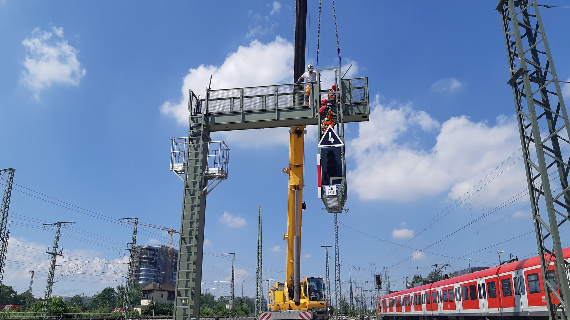 Gelber Kran hebt Signalbrücke zur Montage auf Gleis