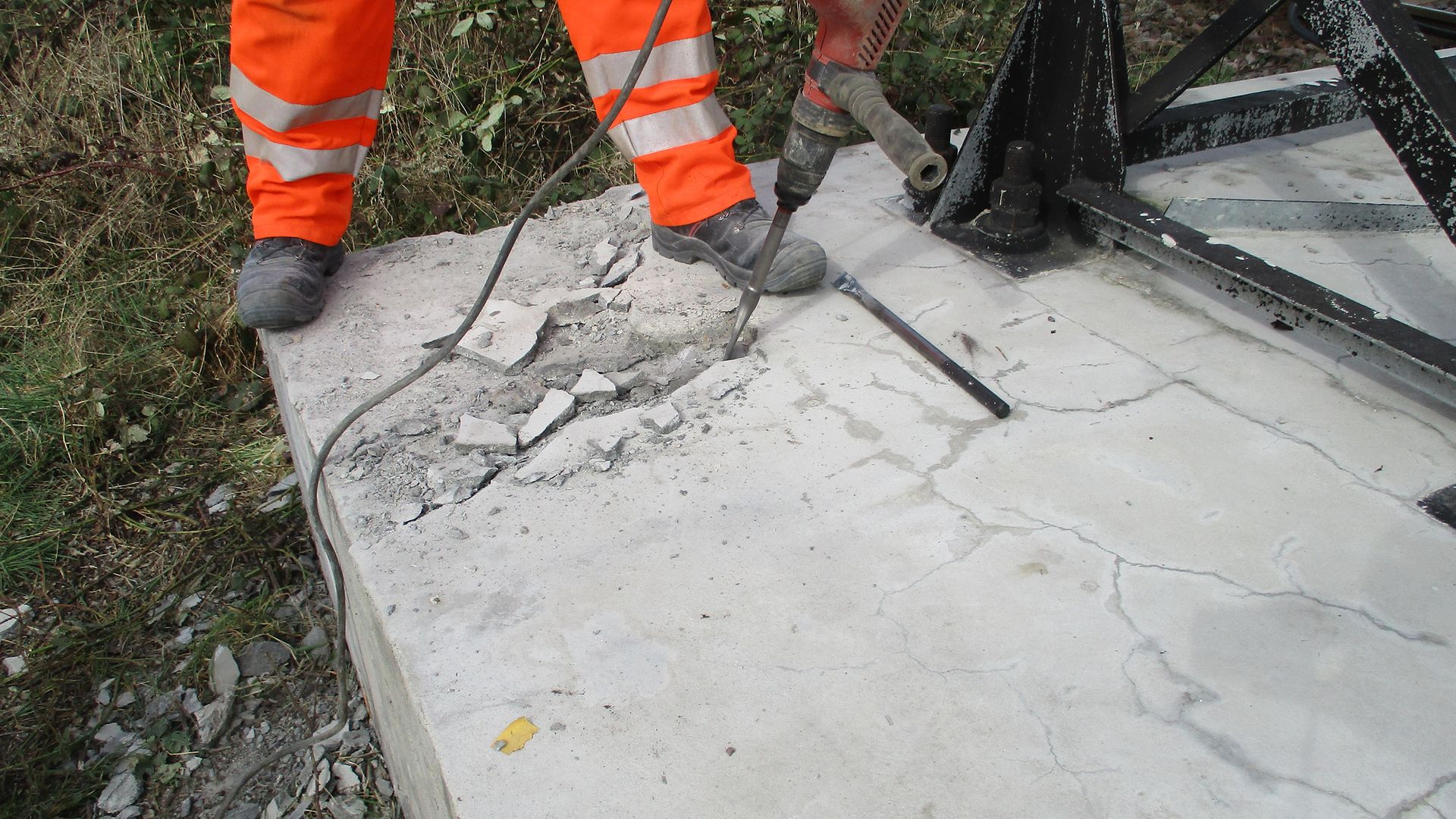 Mitarbeiter saniert Mastfundament, in dem er Beton aufmeiselt.