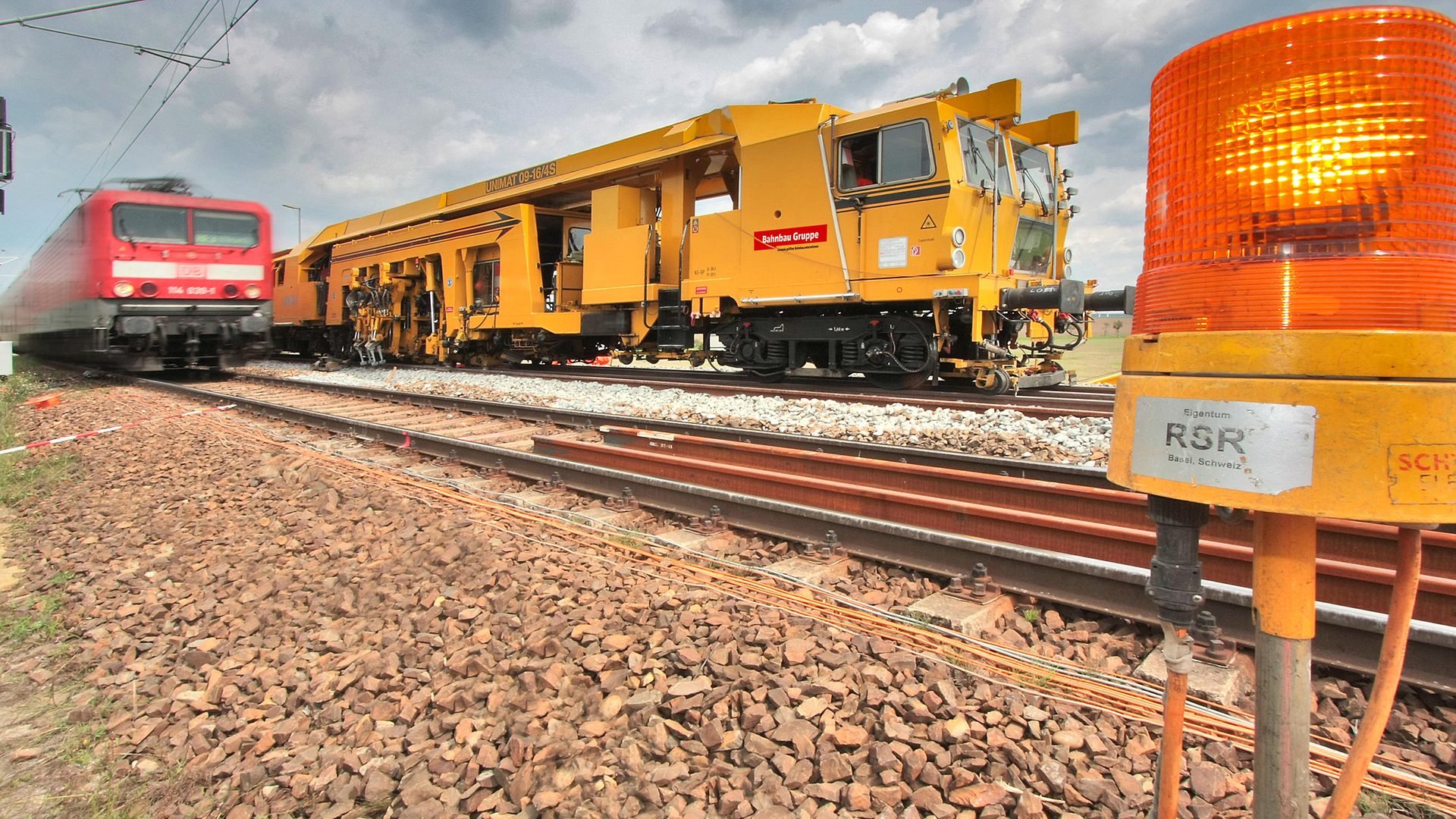 Universalstopfmaschine USM 09-16 4S auf einem Gleis. Auf dem Gleis davor ein Regionalzug