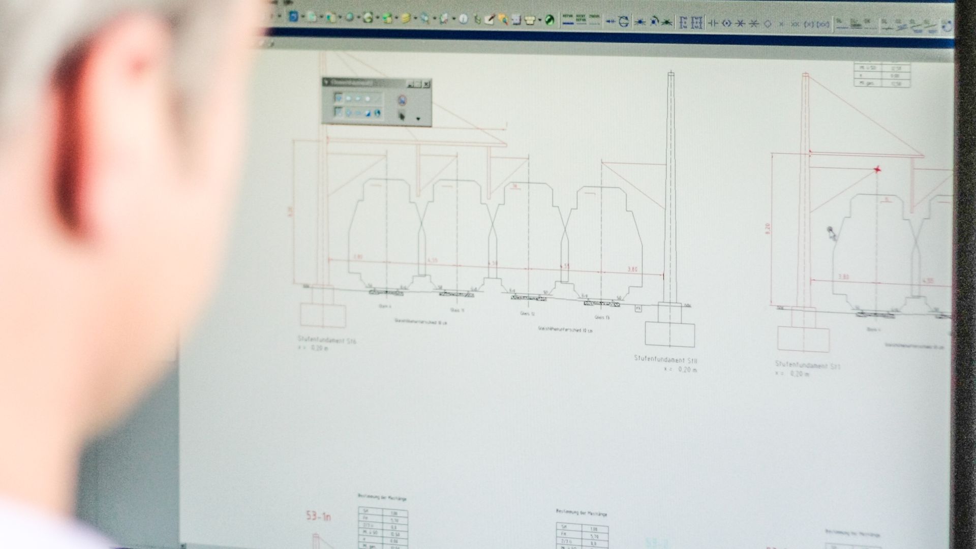 Blick über die Schulter eines Mitarbeiters auf seinem Monitor mit Bauplan.