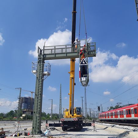 Gelber Kran hebt Signalbrücke zur Montage auf Gleis