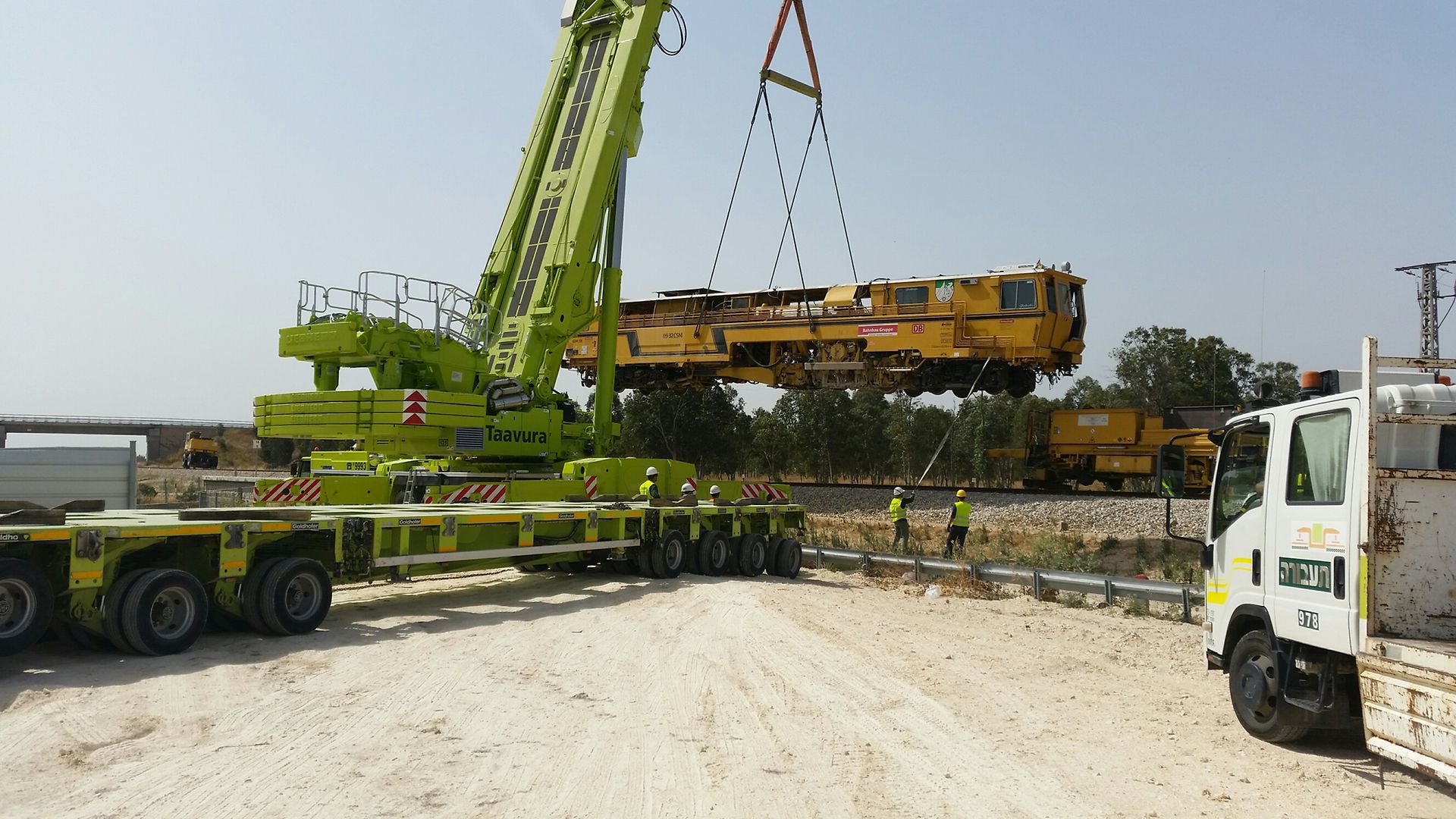 grüner Kran setzt gelbe Baumaschine auf Gleis