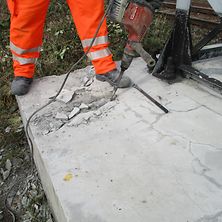 Mitarbeiter saniert Mastfundament, in dem er Beton aufmeiselt.