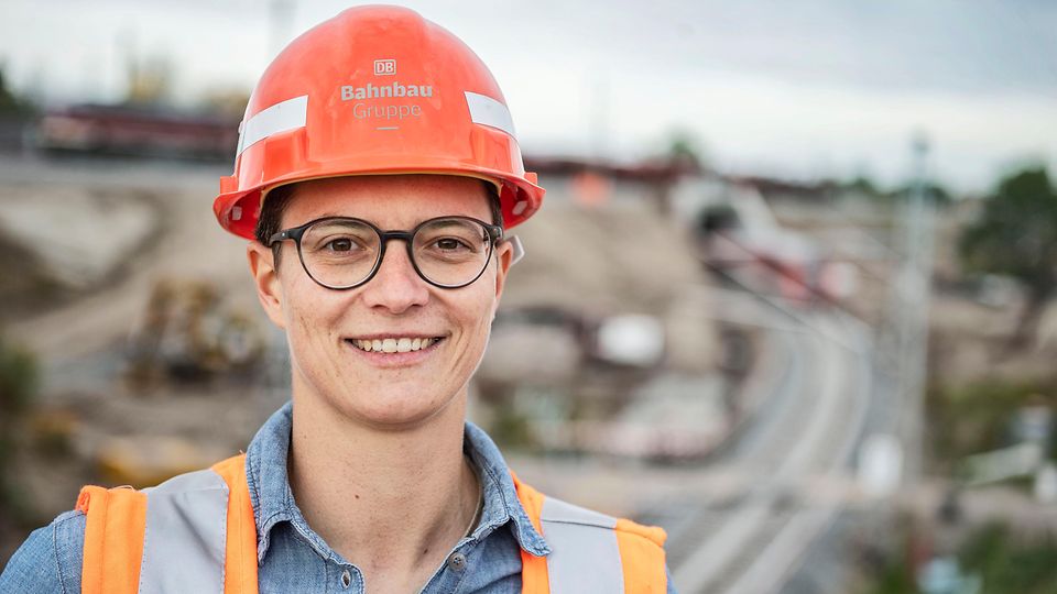 Source: DB Bahnbau Gruppe/Max Lautenschläger Mitarbeiterin mit Helm Großbaustelle im Hintergrund