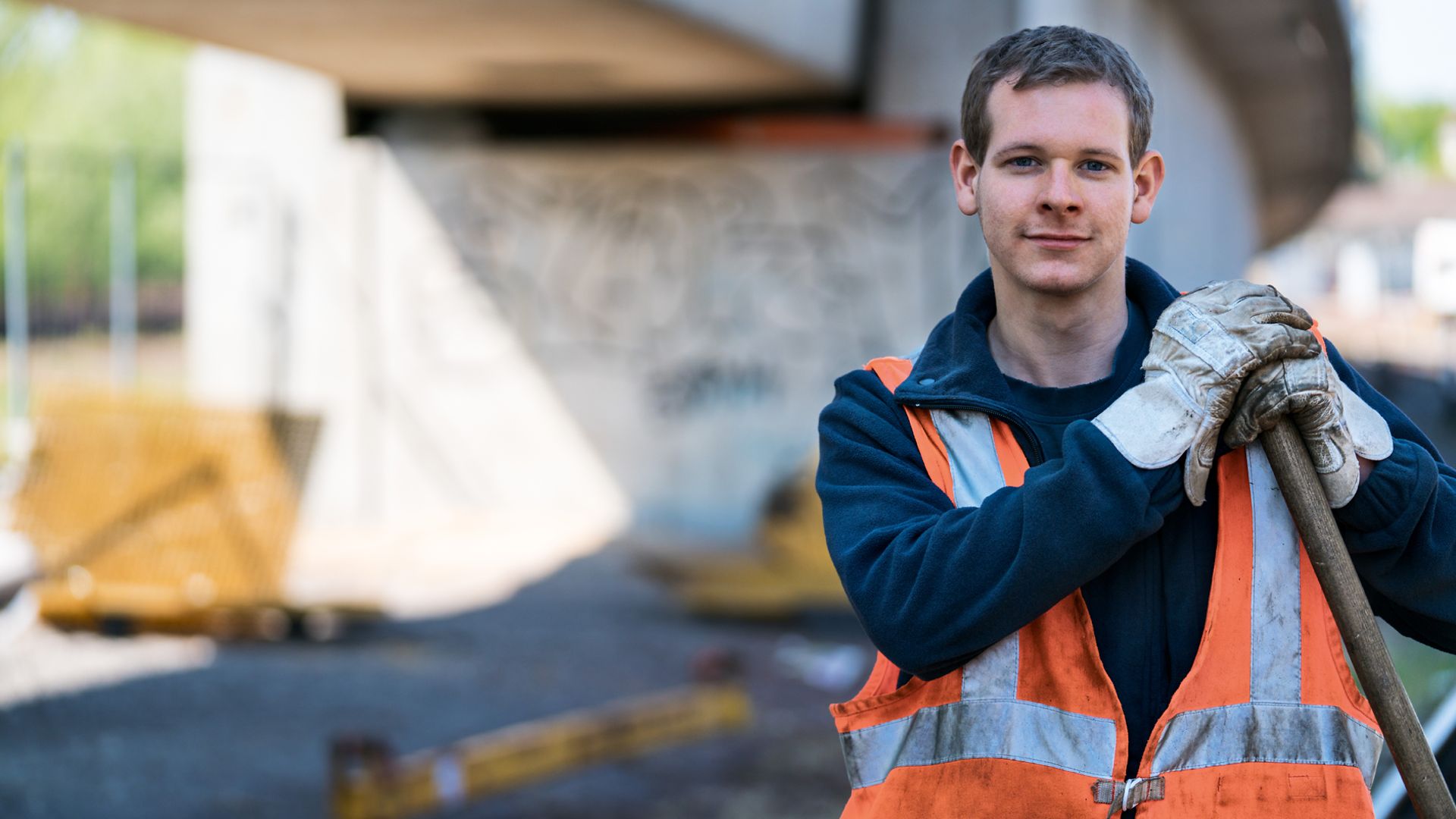 Mann in PSA mit Schaufel unter einer Betonbrücke