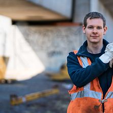 Mann in PSA mit Schaufel unter einer Betonbrücke