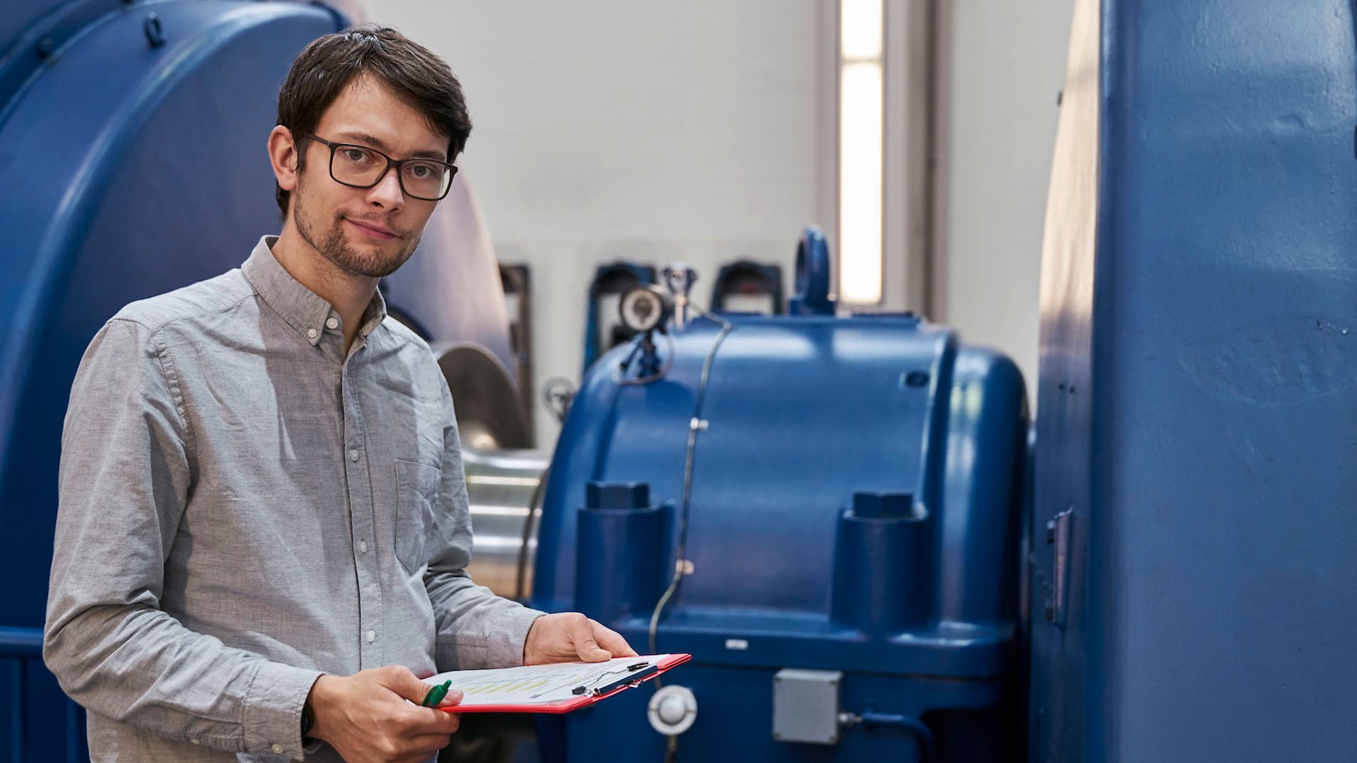 Mann mit Brille und Zettel in der Hand vor einer blauen Turbine