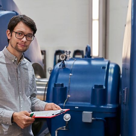 Mann mit Brille und Zettel in der Hand vor einer blauen Turbine